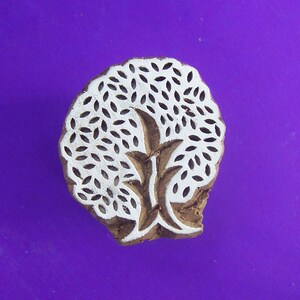 Puede incluir: Un sello de impresión de madera con un diseño de árbol blanco. El árbol está formado por muchas hojas pequeñas.