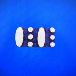 May include: A white and blue ceramic tile with a geometric pattern. The tile has a rectangular shape and is decorated with white circles and a white oval.