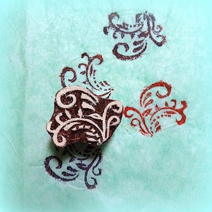 May include: A brown wooden block with a carved floral design. The block is used for stamping patterns onto fabric or paper.