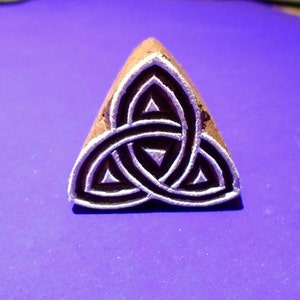May include: A wooden triangle stamp with a white Celtic knot design. The knot is a traditional symbol of love, friendship, and unity.