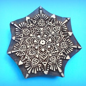 May include: A wooden block printing stamp with a detailed, intricate mandala design in white on a dark brown background. The design features a central flower with radiating petals and geometric patterns.
