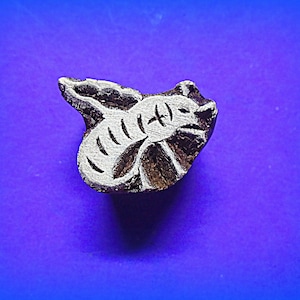 May include: A wooden block carving of a bee with wings outstretched. The bee is carved in a light brown color with white details. The carving is on a purple background.