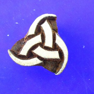 May include: A wooden block stamp with a white Celtic knot design. The stamp is brown and has a triangular shape.