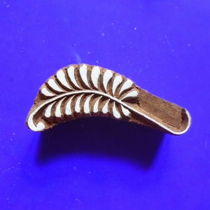 May include: A wooden block printing stamp featuring a white leaf design. The stamp is carved with a detailed leaf pattern and is ready to be used for textile printing.