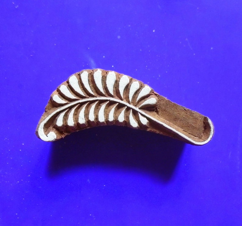 May include: A wooden block printing stamp featuring a white leaf design. The stamp is carved with a detailed leaf pattern and is ready to be used for textile printing.