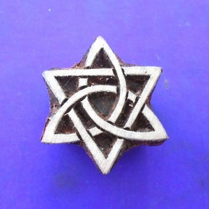 May include: A wooden block printing stamp featuring a six-pointed star design. The star is formed by interlacing lines creating a Celtic knot pattern. The stamp is painted white and has a brown wooden base.