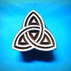 May include: A wooden block carving of a Celtic knot design. The knot is a traditional symbol of interconnectedness and eternity. The carving is painted white and black.
