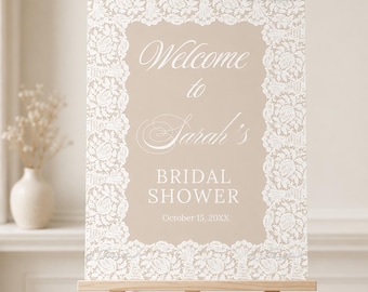 May include: A rectangular sign on a wooden easel featuring a beige background with a white lace border. The text reads: Welcome to Sarah's BRIDAL SHOWER October 15, 20XX. The design uses a mix of script and serif fonts for the event details.