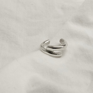 Può includere: Un anello d'argento con un designo semplice e moderno. L'anello è composto da due bande che sono collegate in alto e in basso.