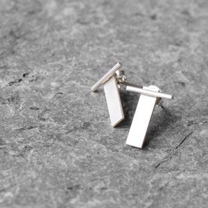 May include: A pair of silver earrings with rectangular shapes and a thin bar extending from the top of each rectangle.