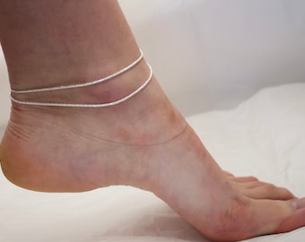 May include: A silver anklet with two delicate chains. The anklet is worn on a person's ankle.