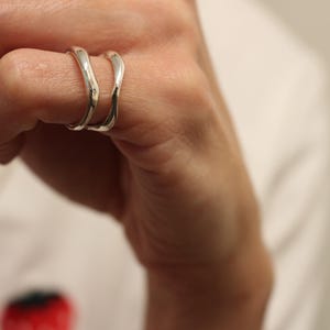 Può includere: Due anelli d'argento con un design ondulato, indossati su un dito.