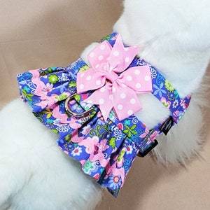 May include: A purple and pink floral dog harness with a pink polka dot bow. The harness has a silver buckle and is designed for small dogs.