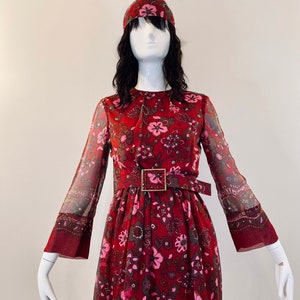 Peut inclure: Une robe longue rouge à manches longues avec un imprimé floral rose et marron. La robe est assortie d'un bandeau rouge et d'une ceinture marron avec une boucle dorée.