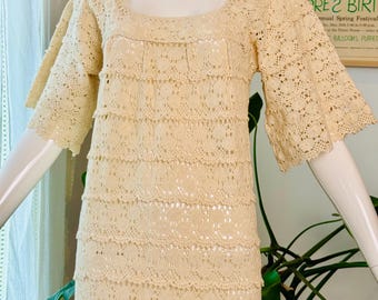 Könnte beinhalten: Cremefarbenes Häkelkleid mit quadratischem Ausschnitt und Stufenrock. Das Kleid hat kurze, ausgestellte Ärmel und ein zartes, offenes Design. Das Kleid wird auf einer Schaufensterpuppe präsentiert und zeigt seinen Vintage-Stil und seine aufwendige Verarbeitung.