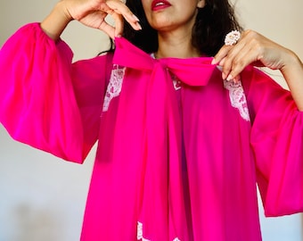 May include: A bright pink sheer blouse with a large bow at the neckline and white lace trim around the collar and sleeves.