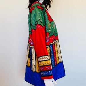 Può includere: Una giacca ricamata colorata con un motivo rosso, verde, blu, giallo e bianco. La giacca ha una manica lunga e una vestibilità ampia.