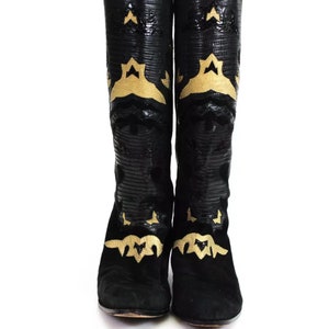 Puede incluir: Botas negras de ante hasta la rodilla con adornos en forma de estrella dorada.