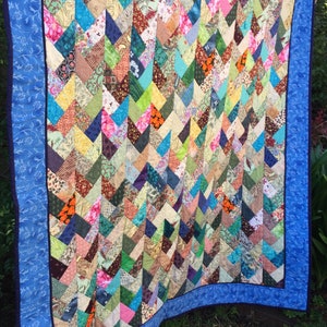 May include: A colourful patchwork quilt with a chevron pattern. The quilt is edged with a blue fabric with a floral design.