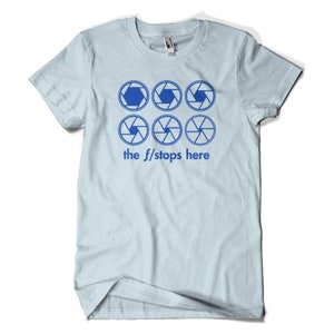 Könnte beinhalten: Hellblaues T-Shirt mit sechs blauen Kamera-Blenden-Symbolen und dem Text "the f/stops here".