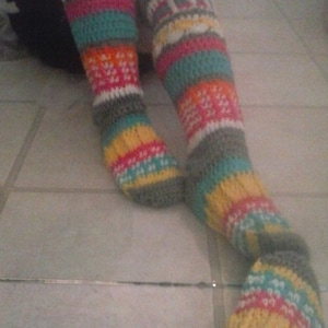 May include: A pair of colorful crocheted leg warmers with a flower embellishment. The leg warmers are made with a variety of colors, including gray, teal, pink, yellow, and white.