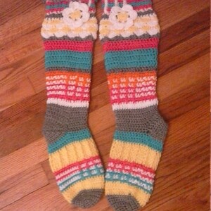 May include: A pair of colorful crocheted knee-high socks with a flower design. The socks are striped with grey, teal, pink, orange, and yellow.