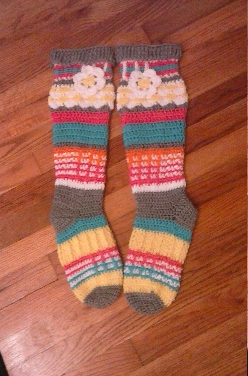 May include: A pair of colorful crocheted knee-high socks with a flower design. The socks are striped with grey, teal, pink, orange, and yellow.