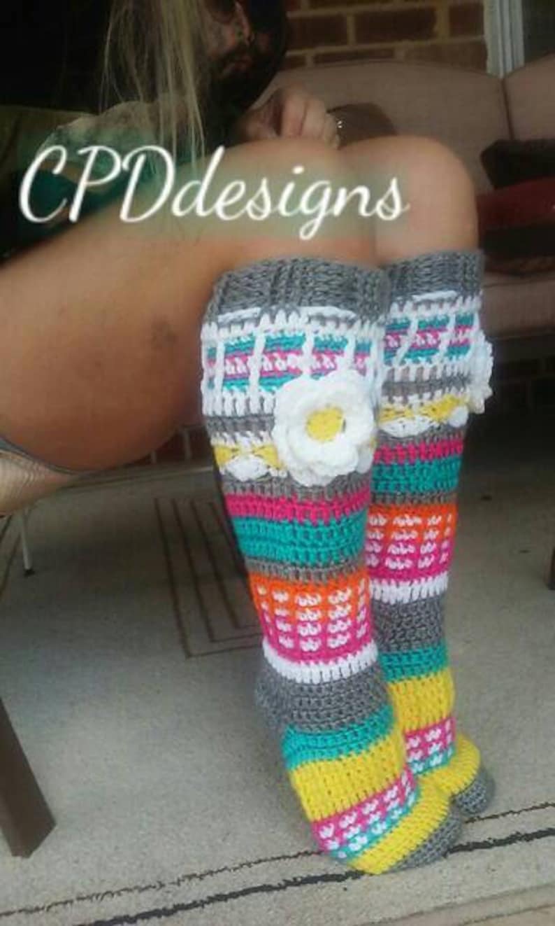 May include: A pair of colorful crocheted leg warmers with a white flower accent. The leg warmers are striped with grey, turquoise, yellow, orange, and pink.