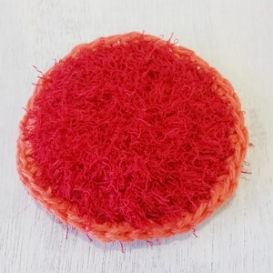 May include: A red and orange crocheted dish scrubby. The scrubby is round and has a textured surface.