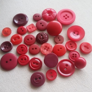 May include: A collection of red and burgundy buttons of various sizes and shapes.