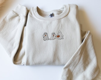 May include: A light grey sweatshirt featuring a design of three ghosts holding pumpkins. The ghosts have black eyes and mouths.
