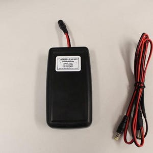 May include: A black electronic device with a white label that reads "Danisha Farms Hand-Watering System 618-664-1383 www.danishafarms.com". The device is connected to a black and red wire.