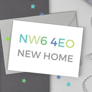 May include: A white card with the text "NW6 4EO NEW HOME" in green, blue, and grey. The card is inside a grey envelope, with a dark grey envelope behind it. Star-shaped confetti in green and blue adds a decorative element.