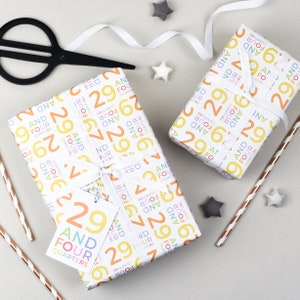 May include: Two white gift boxes wrapped in colorful wrapping paper with a pattern of the number 29 and the words "And Four Quarters". The boxes are tied with white ribbon and have a gift tag with the same pattern.