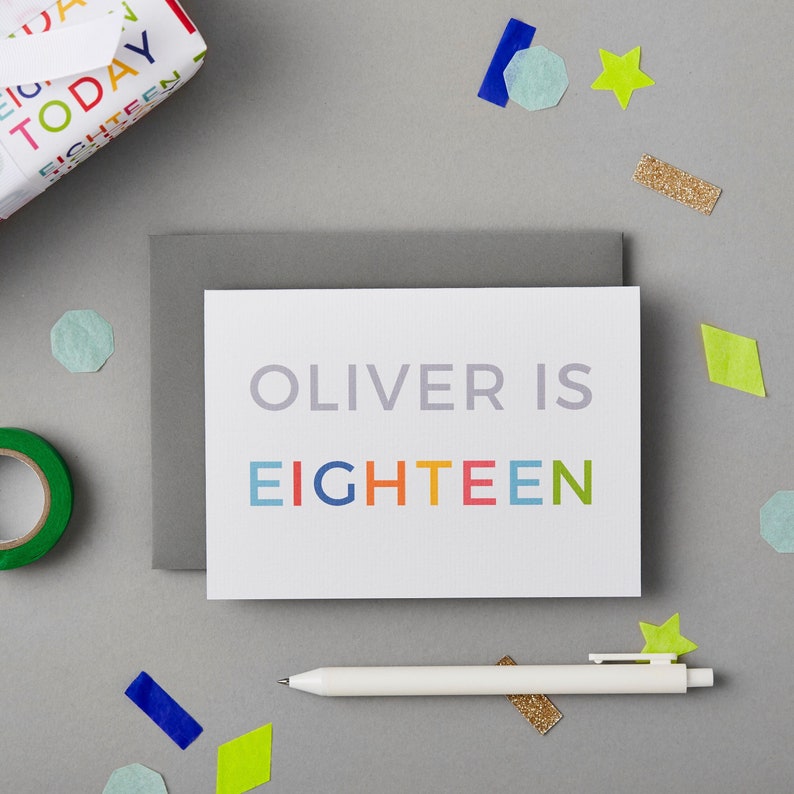 May include: A white card with a gray envelope. The card has the text "Oliver is Eighteen" in rainbow colors. The card is surrounded by confetti.