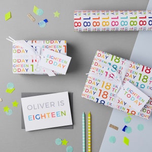 May include: Two wrapped gifts with colorful "Eighteen Today" wrapping paper. A gray card with the text "Oliver is Eighteen" in colorful letters.  Two striped candles and confetti.