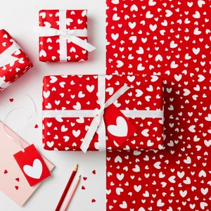 May include: Red and white wrapping paper with a heart pattern. The paper is wrapped around a gift box with a white ribbon and bow.