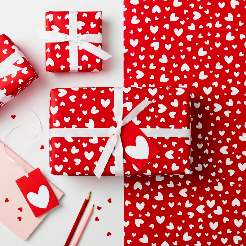 May include: Red and white wrapping paper with a heart pattern. The paper is wrapped around a gift box with a white ribbon and bow.