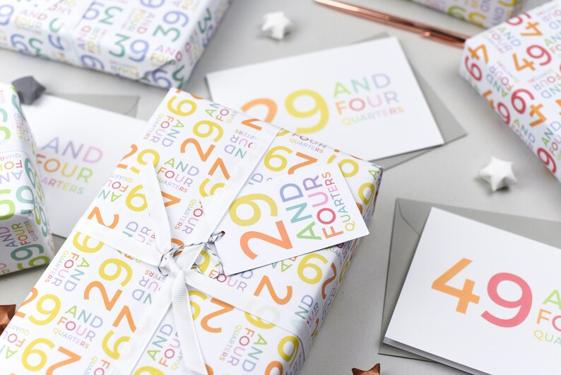 May include: A gift wrapped in white paper with a colorful pattern of numbers and the words "And Four Quarters". The gift is tied with a white ribbon and a tag that says "29 And Four Quarters".