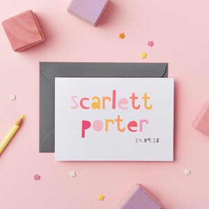 May include: A white card with the name "Scarlett Porter" in colorful, bold letters. The date "14.09.18" is printed below the name. The card is surrounded by pink and yellow stars and wooden blocks.