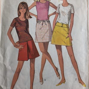 Puede incluir: Patrón de costura vintage con tres conjuntos de mujer. Los conjuntos incluyen un top a rayas y una falda roja, una camiseta sin mangas rosa y una falda a cuadros, y un top a rayas con una falda amarilla. El patrón está etiquetado como "Junior Talla 13, Contorno de pecho 84 cm."