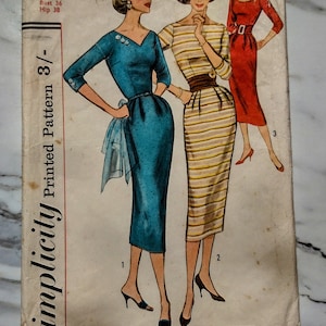 Op de afbeelding: Vintage Simplicity naaipatroon nummer 2153 voor een jurk. Het patroon is voor maat 16, borstomvang 36 en heupomvang 38. Het patroon toont drie verschillende jurkstijlen, een in blauw, een in geel-witte strepen en een in rood. Het patroon is gemarkeerd met "Eenvoudig te maken."