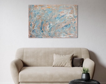 May include: Abstract painting with a blend of blue, peach, and white brushstrokes. The artwork is displayed above a beige sofa with a matching throw pillow. A black, round side table and a small plant in a black pot complete the scene.