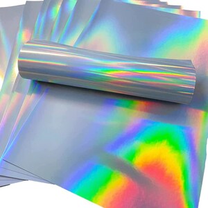 May include: A stack of iridescent holographic sheets in a silver color with a rainbow sheen. The sheets are rolled up and stacked on top of each other.