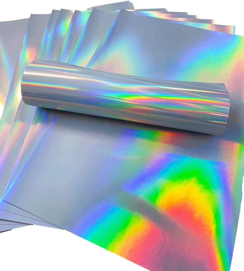 May include: A stack of iridescent holographic sheets in a silver color with a rainbow sheen. The sheets are rolled up and stacked on top of each other.