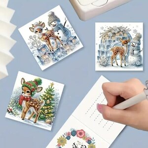 May include: Three Christmas cards featuring a winter scene with a deer and a snowman. The cards are blank inside for writing a message.