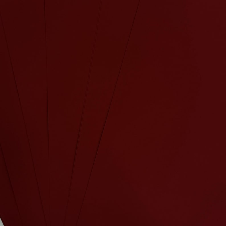 May include: A fan of several sheets of deep burgundy paper. The paper has a smooth, matte finish and is arranged to create a fanned-out effect. The color is a rich, dark red, with subtle variations in tone across the sheets.