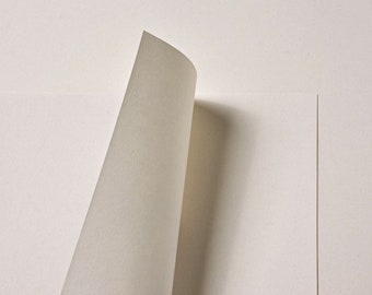 May include: Close-up of off-white paper with a textured surface. The corner of a sheet is curled, revealing the edge and its shadow. The paper's neutral colour suggests suitability for artistic or office applications.