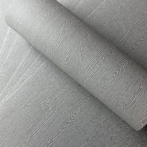 May include: A roll of gray wallpaper with a wood grain pattern. The wallpaper has a textured surface with visible wood grain lines and knots. The color is a neutral gray, suitable for various interior design styles.