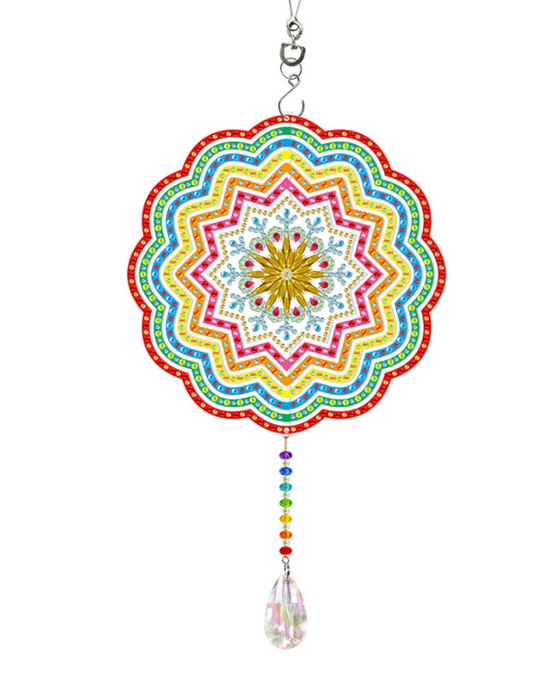 May include: A colorful rainbow mandala with a crystal teardrop hanging from it. The mandala is made of rhinestones and has a snowflake design in the center.